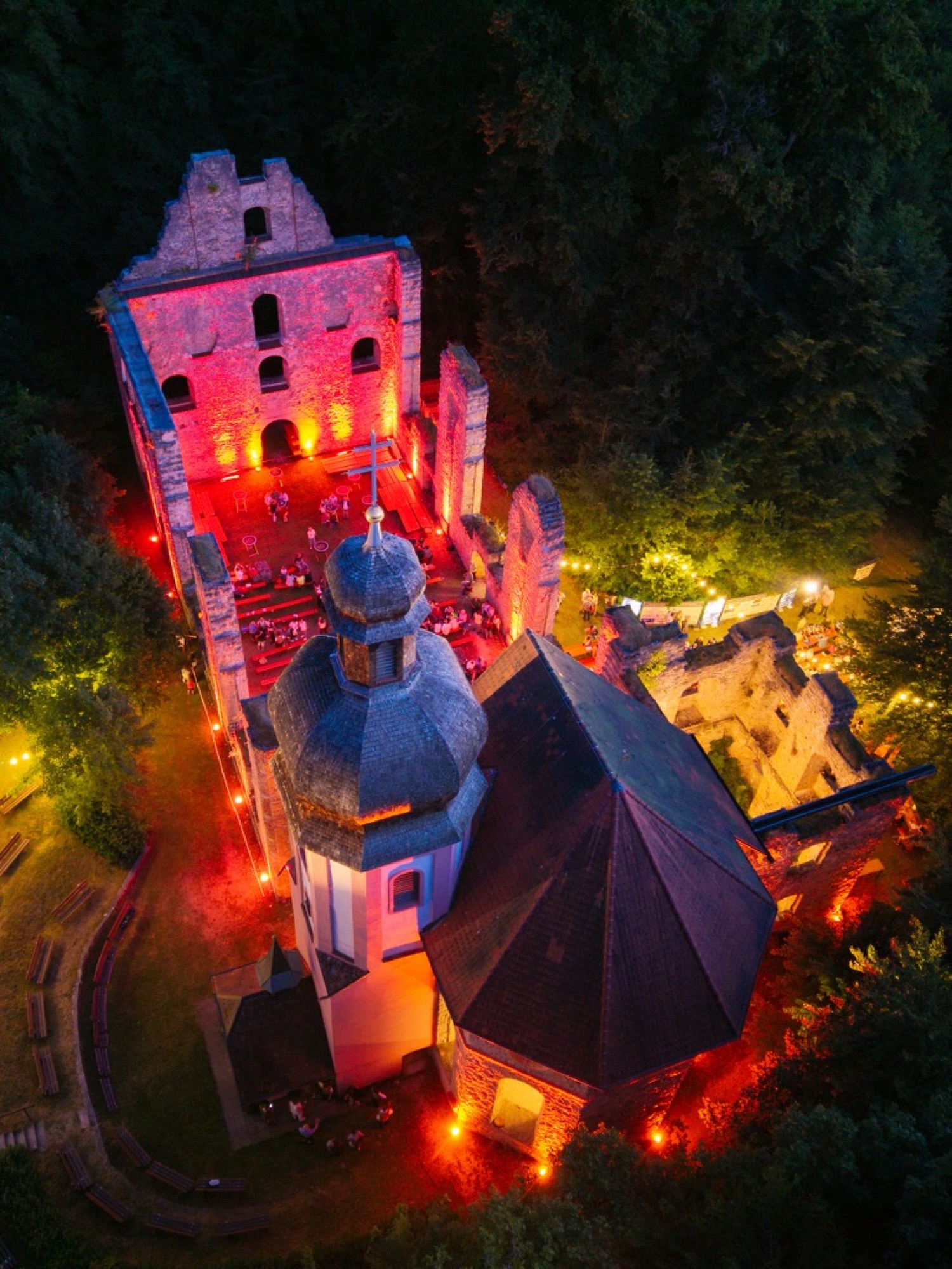 Nachts rot illuminierte Klosterruine mit Besuchern bei einer Abendveranstaltung