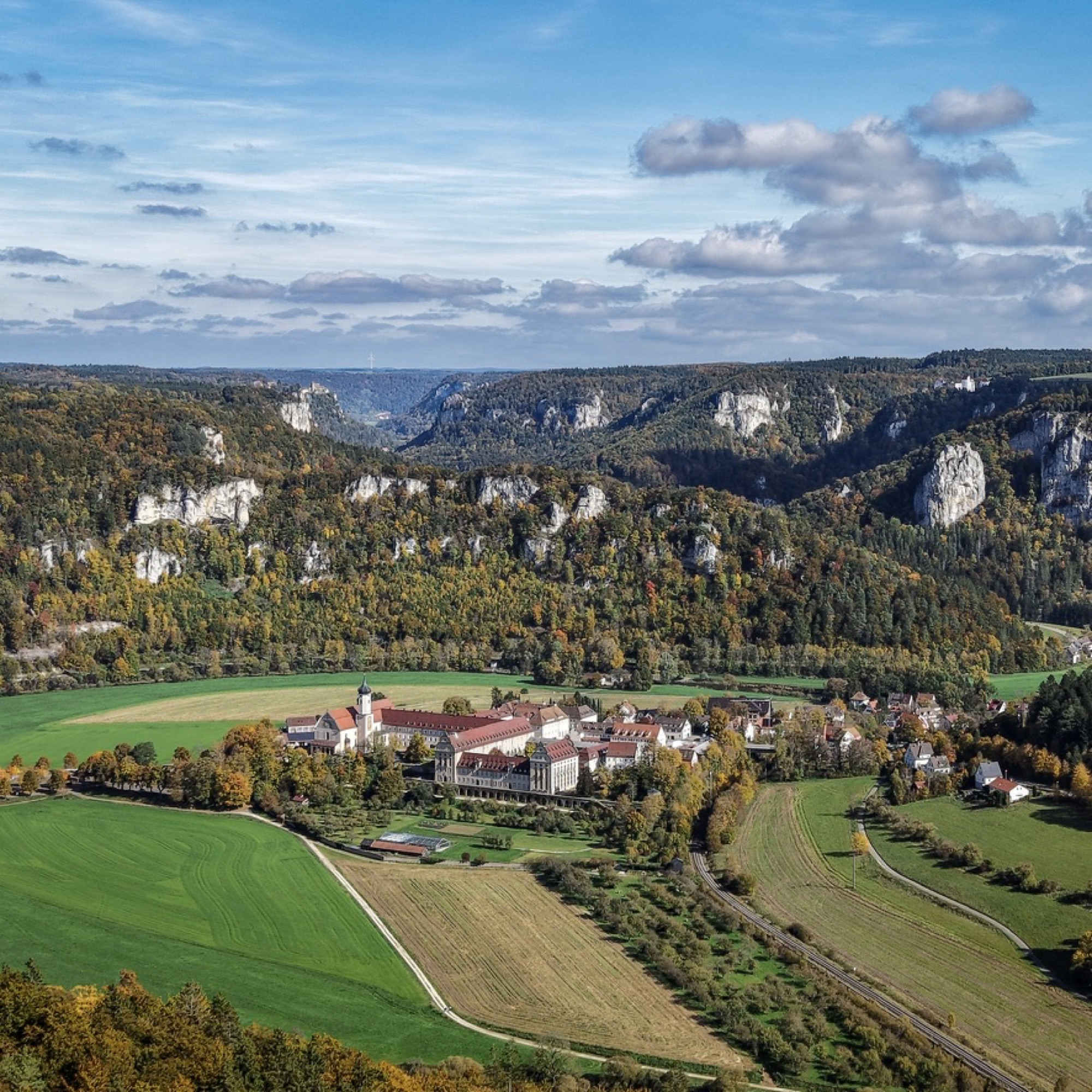 Barockkloster im herbstlichen Tal, umgeben von Feldern und bewaldeten Hügeln